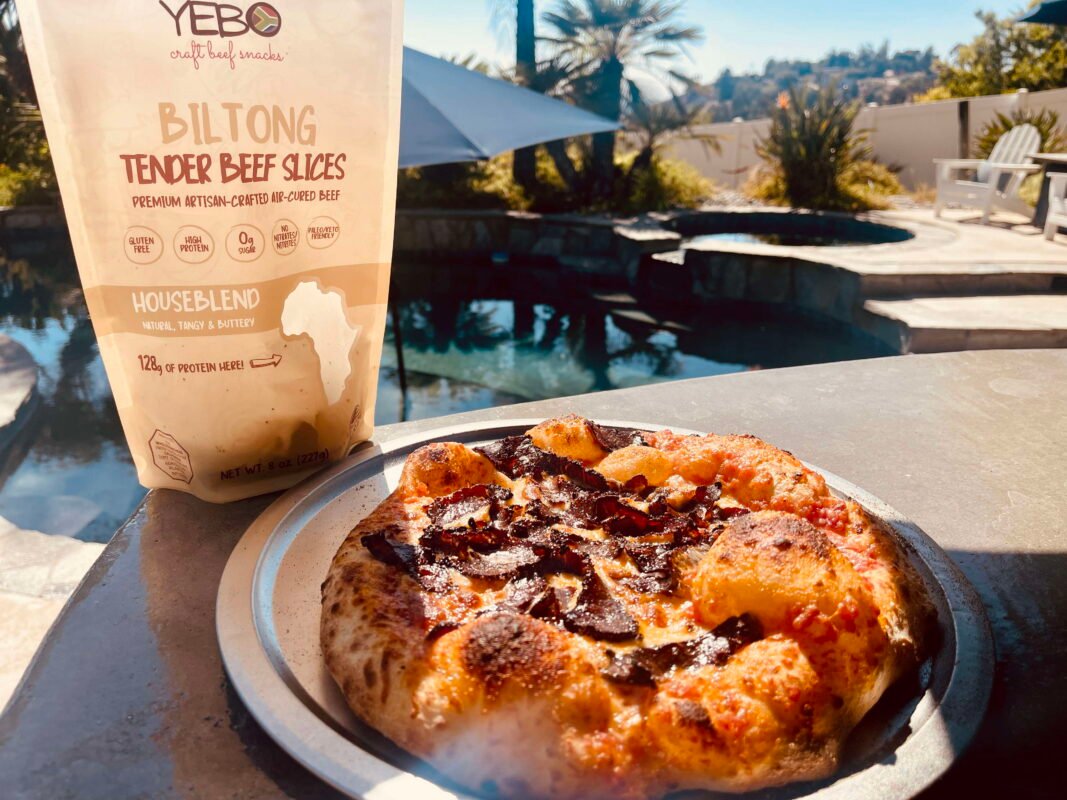 Fresh biltong pizza by the poolside with artisan beef slices and golden crust.
