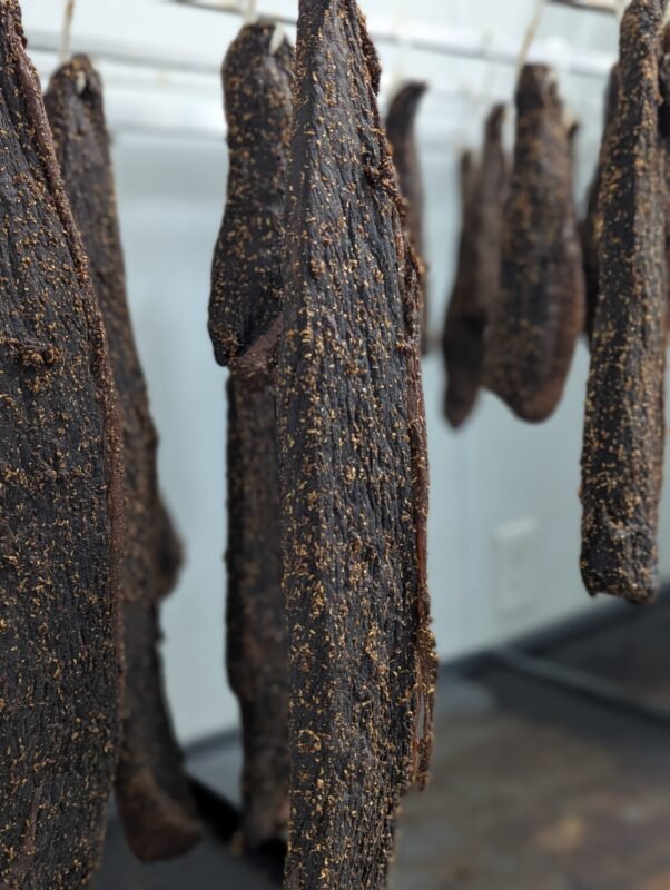 Hanging strips of seasoned beef biltong drying in a professional meat curing room.