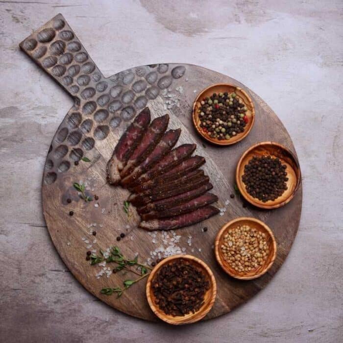 A cutting board with sliced biltong and different spices on it