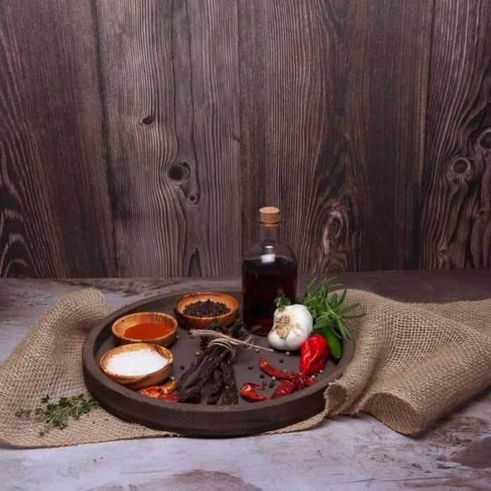 A round wooden plate with chilibites, spices and herbs on it