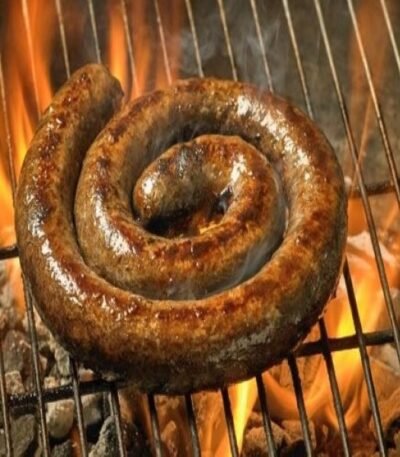 Coiled boerewors sausage grilling over open flames on a barbecue with glowing coals.