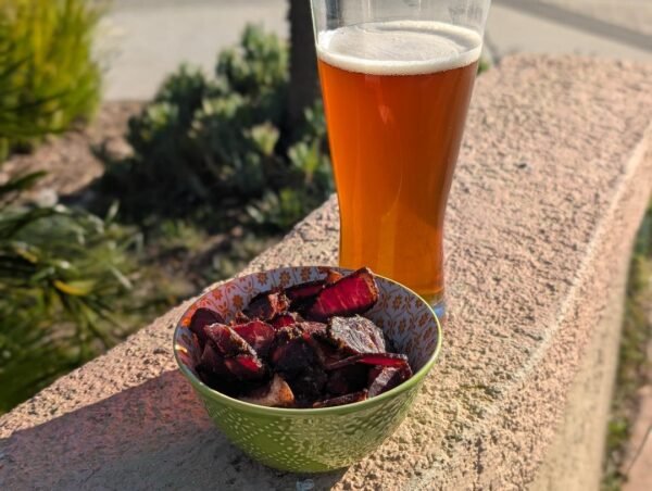 Biltong in patterned bowl with amber beer on stone ledge in sunlight.