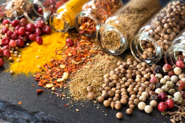Vibrant colorful spices and seasonings spilled from glass jars on dark stone background.
