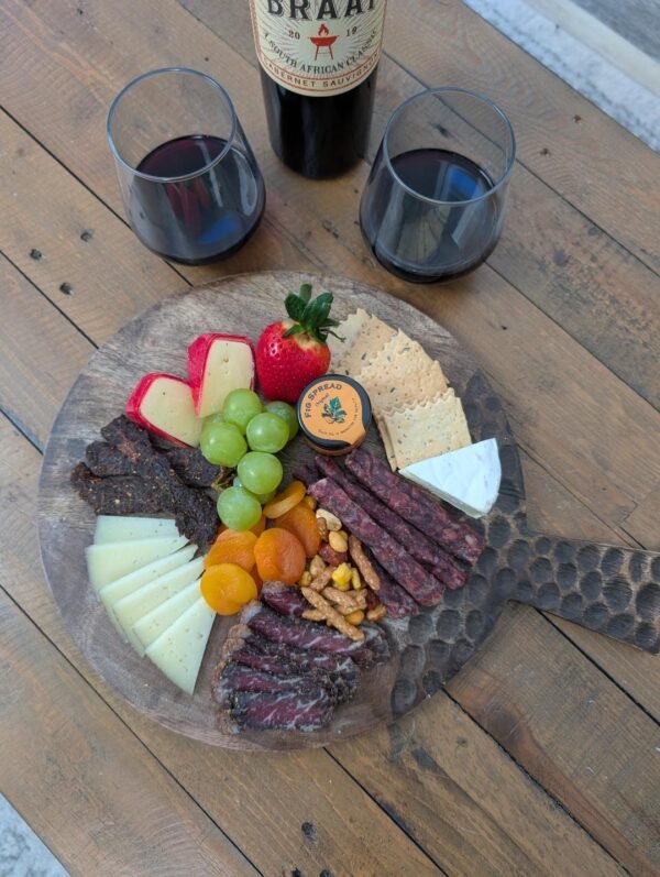 Rustic charcuterie board with biltong, cheese, fruit, and red wine pairing.